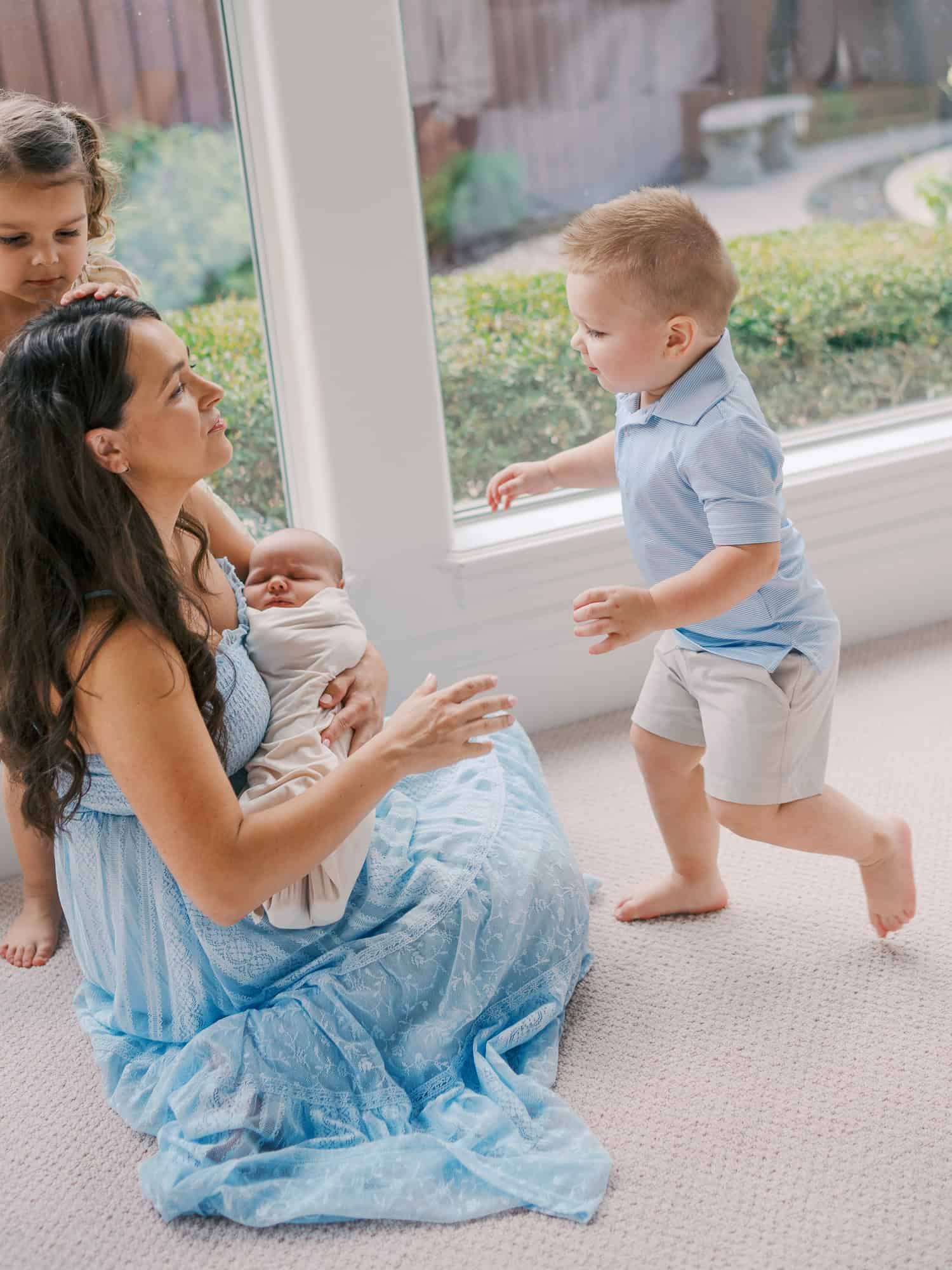mom holding newborn baby in Plano home with kids running up to hug her