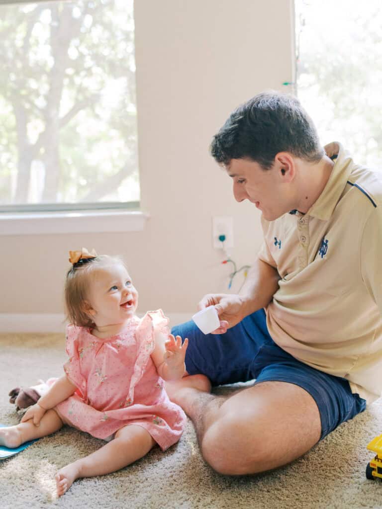 dad and toddler daughter sharing a cup of pretend tea in bright room together smiling at each other