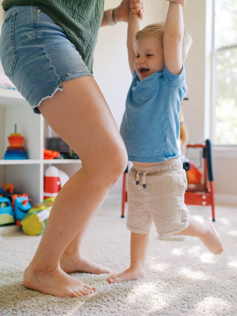 closeup of legs of mom and son jumping together in playroom with speckled light coming from behind