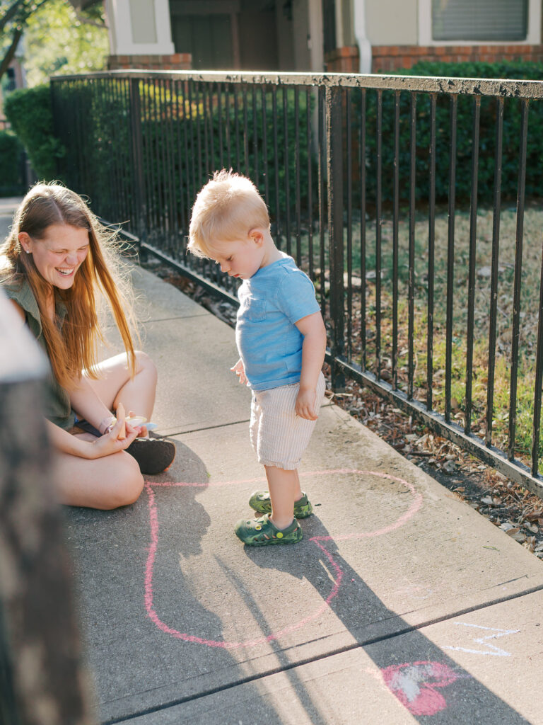 mother and son smiling at each other on sidewalk drawing a heart with pink chalk