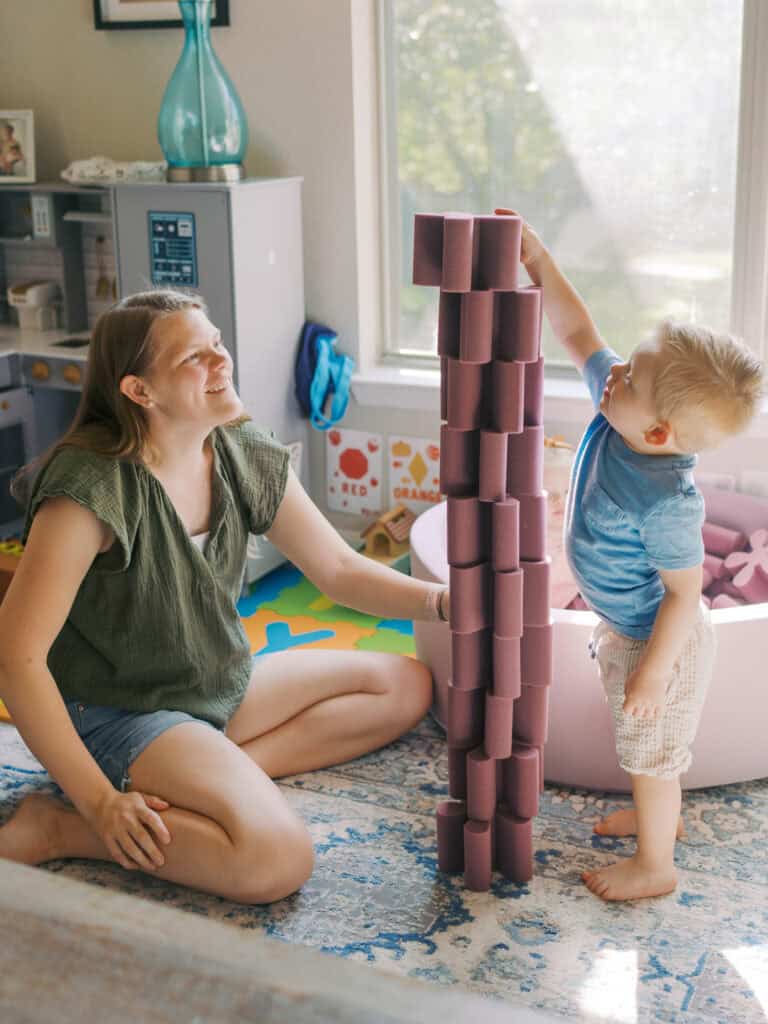 mom and son building a foam block tower in their living room with bright windown behind