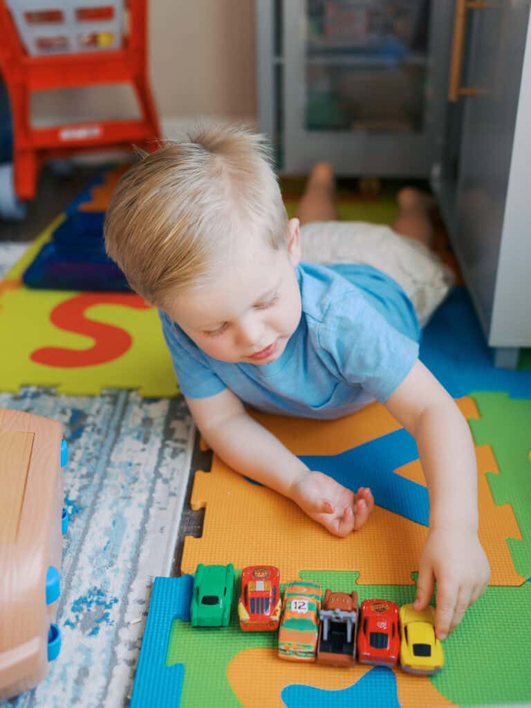 toddler boy lining up several toy race cars on his play mat